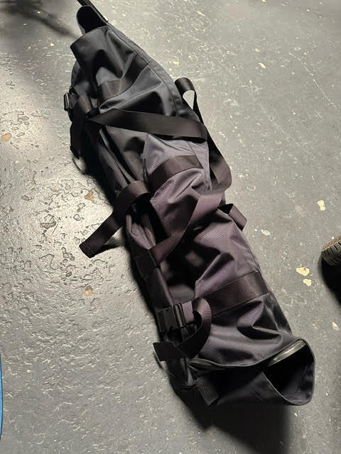 大型カメラ三脚を収納したコーデュラナイロン1680製撮影機材用バッグ。バックル付き固定ベルトでしっかりとまとめた外観